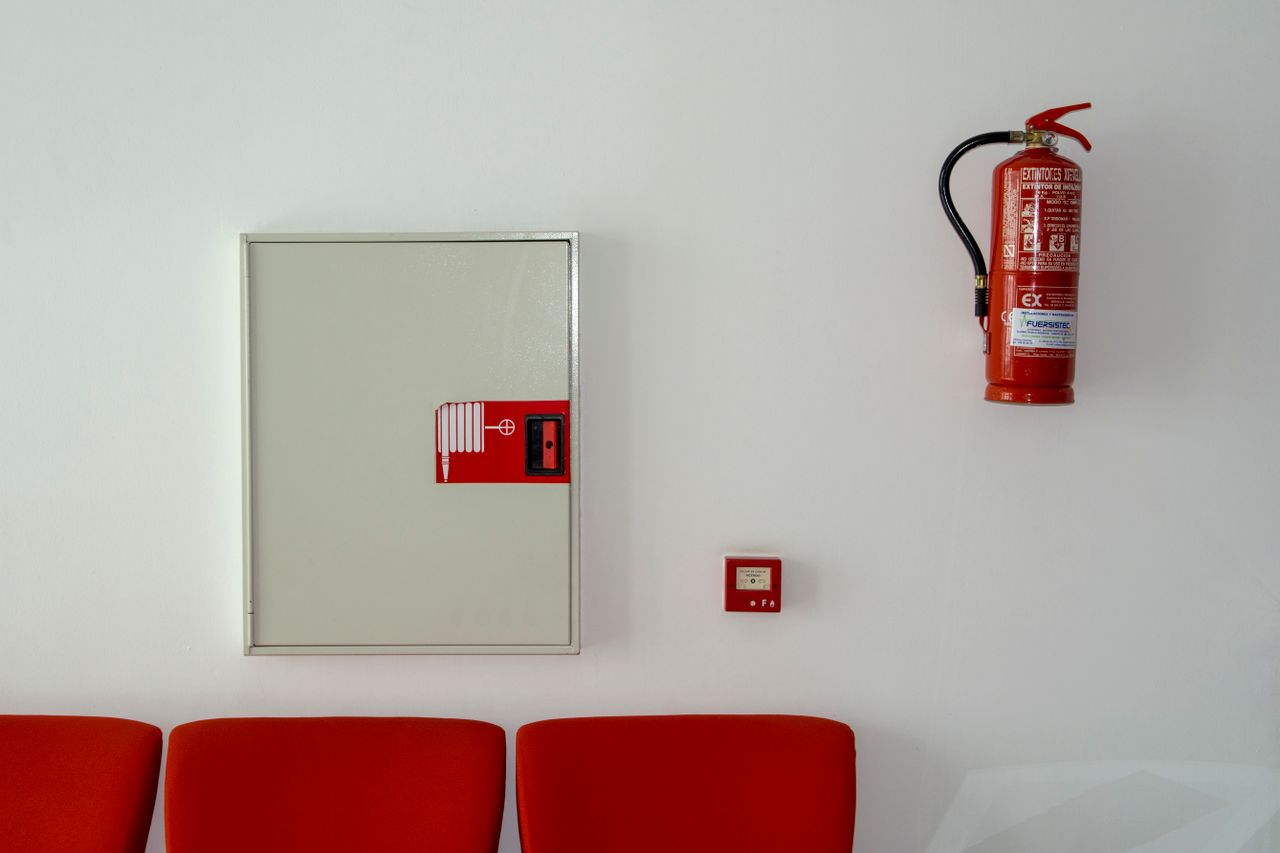why-choose-us Fire extinguisher and safety equipment mounted on a white wall with red seating below.