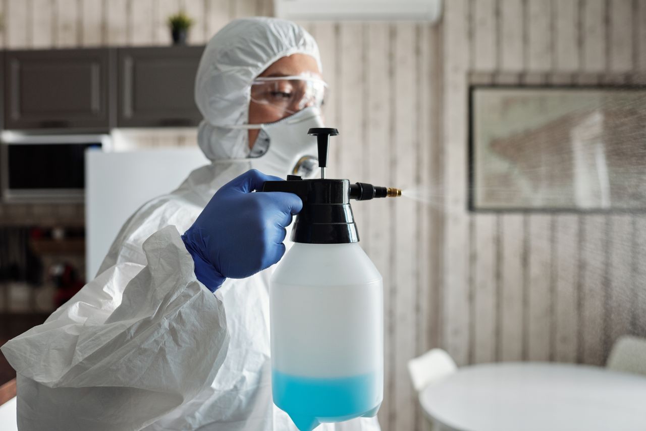 team-01 Professional in full gear disinfecting indoor area using a spray bottle for COVID-19 prevention.